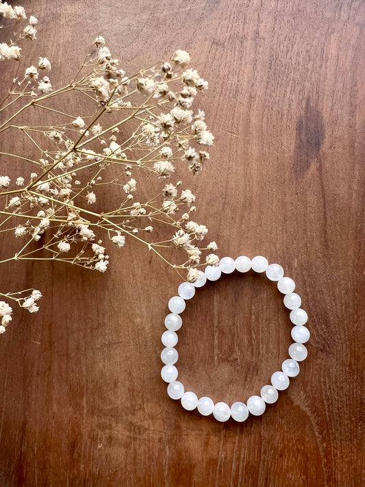 White beaded bracelet on a wooden surface with dried white flowers.